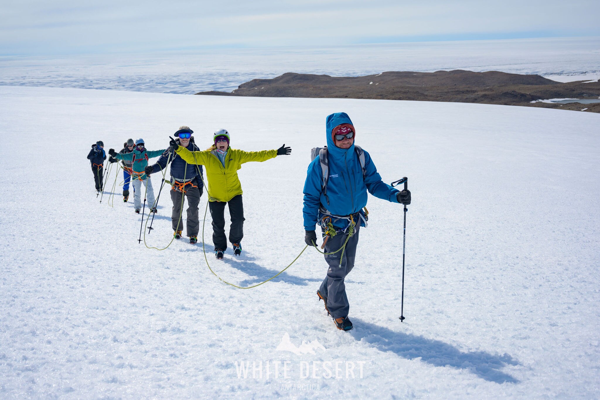 A group of six people trek through the snow tied together for support in Antarctica. 