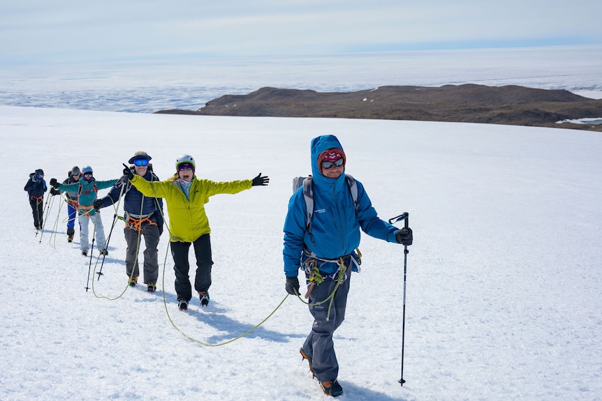 A group of six people trek through the snow tied together for support in Antarctica. 