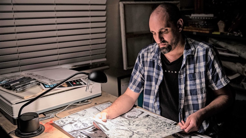 Safdar Ahmed sitting at a desk in his studio with his artwork