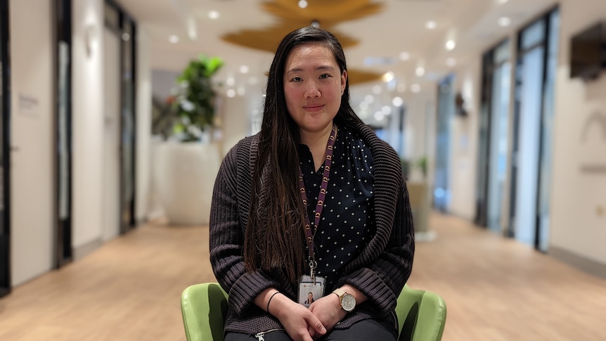 Natalie Wo sits on a green chair in the centre of the photo inside Midland Head to Health