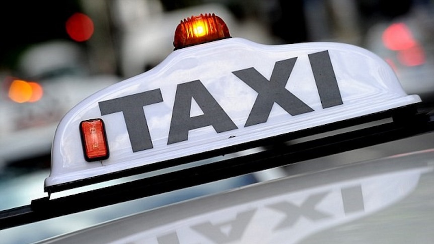 A lit sign saying 'Taxi' sits on the roof of a vehicle