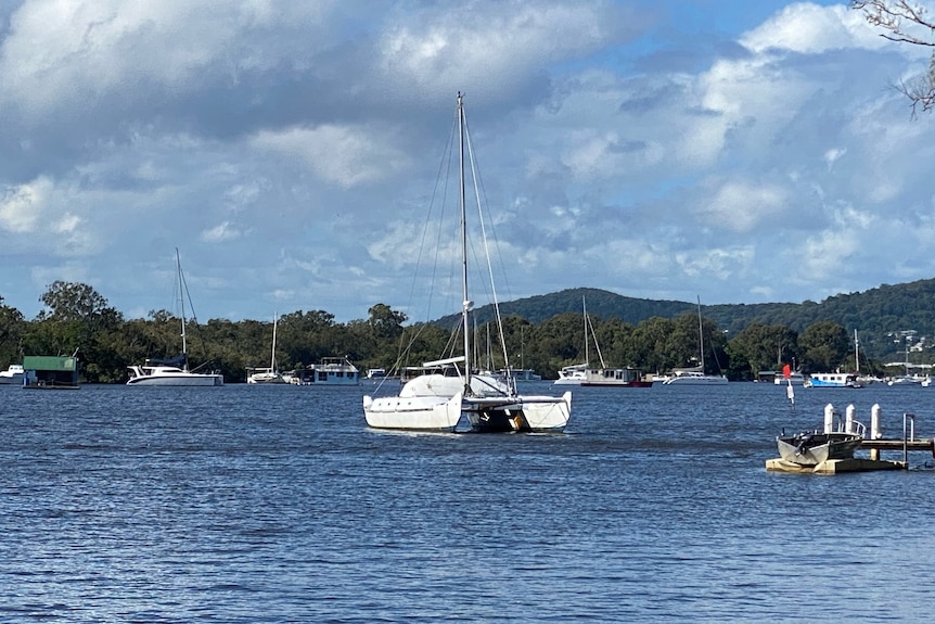 Boats on a blue river, with small mountains and a cloudy blue sky in the background.