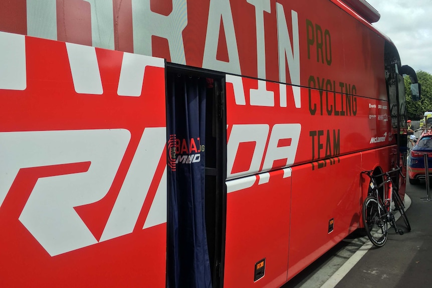 A black racing bicycle is pictured next to a red bus which makes it look giant by comparison.