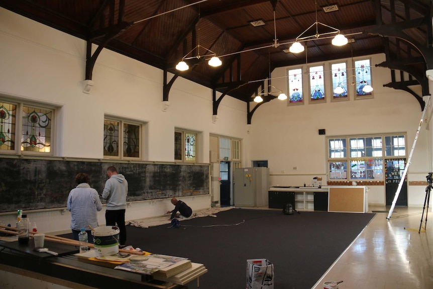 A large room with vaulted ceiling, stained glass windows and a long chalkboard along one wall with signs of renovations.