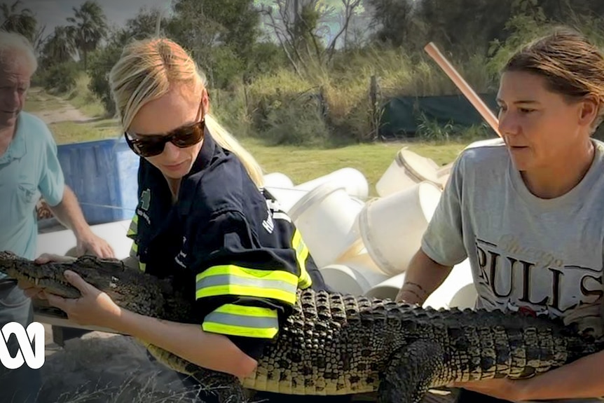 two women hold a small crocodile