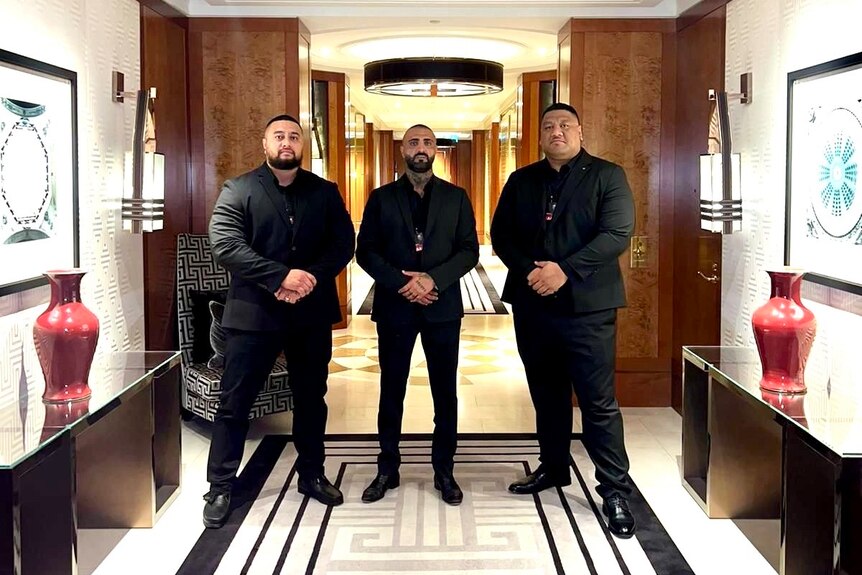 Three bodyguards standing in a hallway.