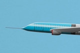 You view a cartoon image of a syringe in the shape of a plane flying against a blue sky.