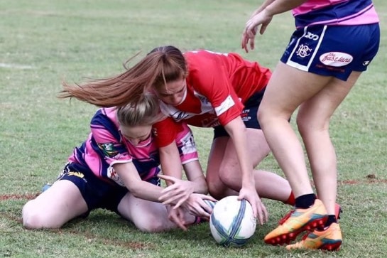 Two girls reach for a football while a third stands above.