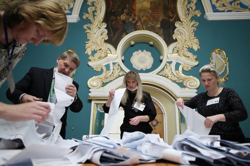 A group of people sift through paper ballots.