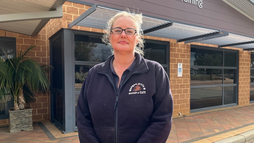 A woman wearing glasses stands outside a bank