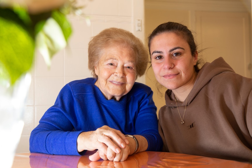 An older woman and a younger woman sitting at a table and smiling at the camera.