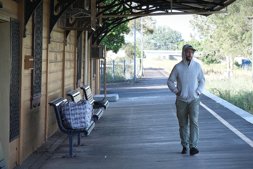 A young man with brown beard wearing a white hoodie and walking along old railway platform