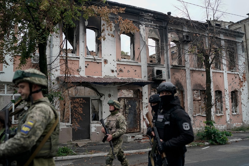 Ukrainian servicemen walk past heavily damaged buildings.