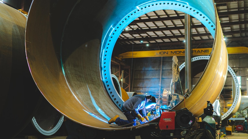 Man wears wielding mask and works inside a massive tube.