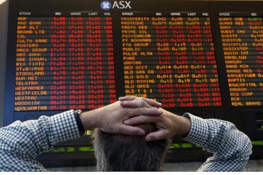 A man stands with his hands on his head looking at the ASX numbers.