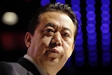 Meng Hongwei wears a suit and stands in front of a black and purple background