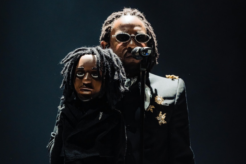 Kendrick Lamar performs live holding a mini-puppet version of himself under spotlight