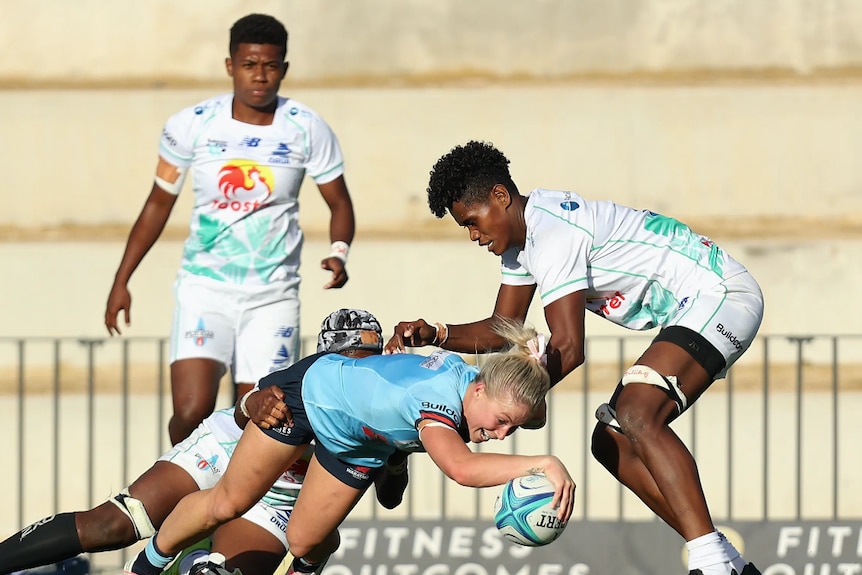 A woman is tackled as she scores a try during a rugby match 