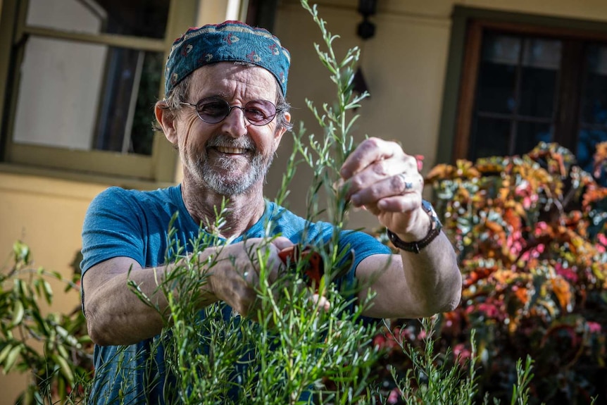 Karl Schurr smiles while pruning a plant in his garden.