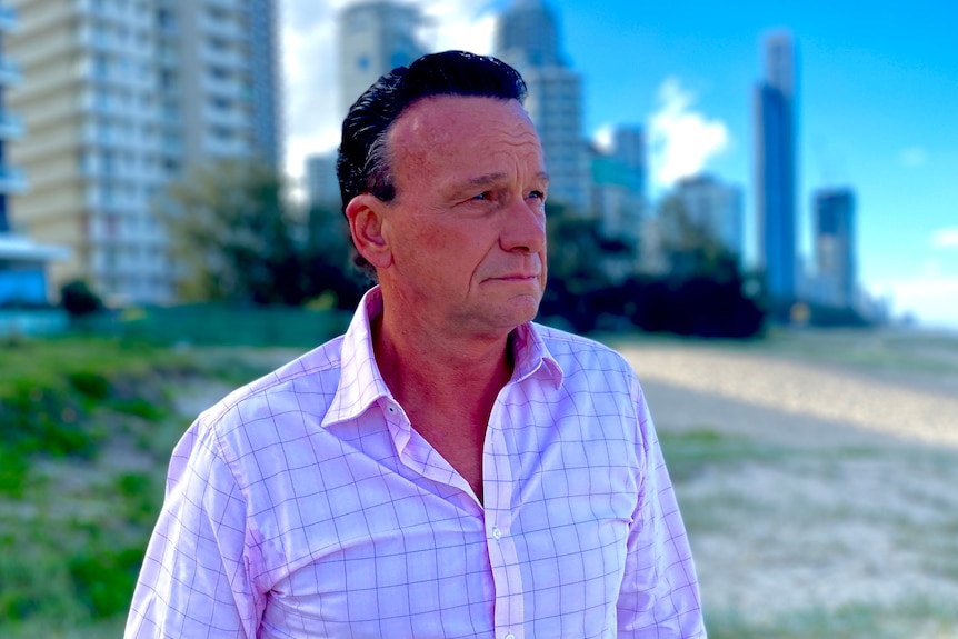 A man in a pink shirt stands on a beach with apartment buildings in background.