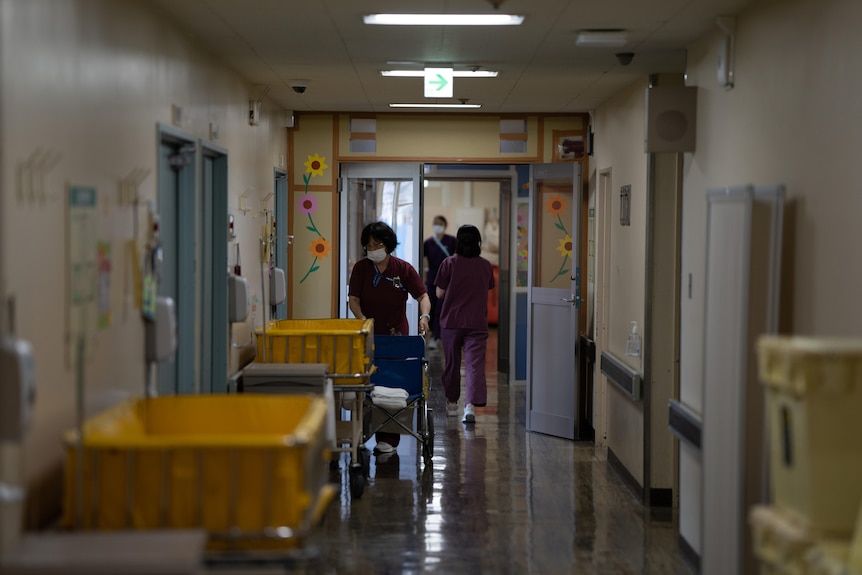 Three nurses in burgundy scrubs walking down a paediatric hospital ward 