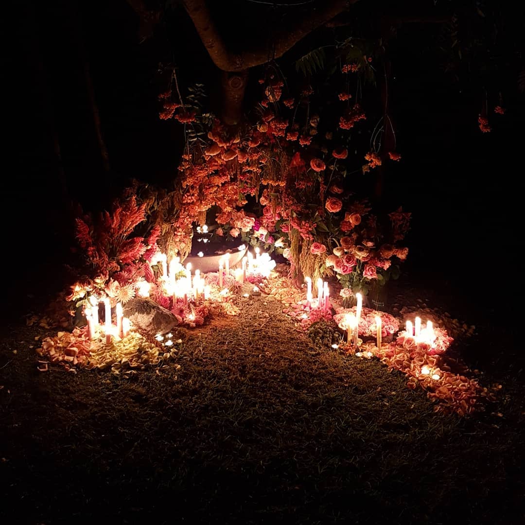 A night shot of flowers and candles arranged in a triangle shape.