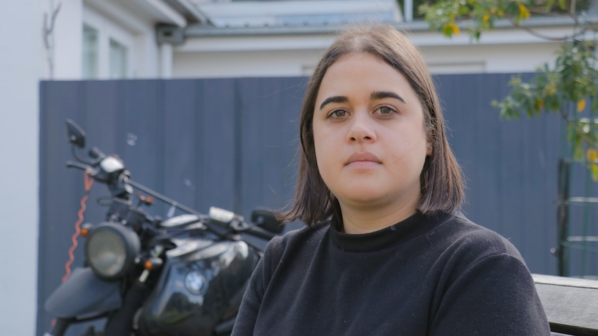 Caitlin Scaife sits in an urban park for a story about underpayment at work.