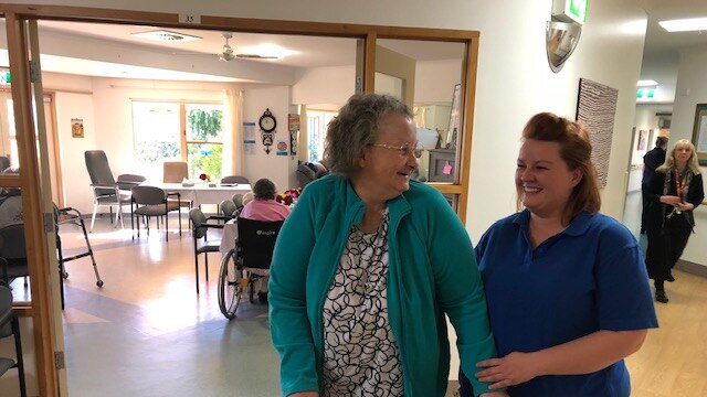 A hospital worker stands with a resident at an aged care facility.