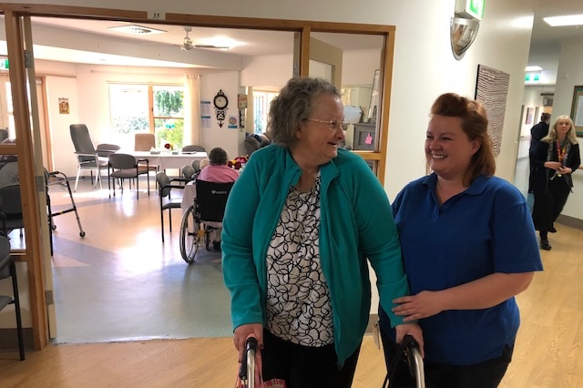 A hospital worker stands with a resident at an aged care facility.