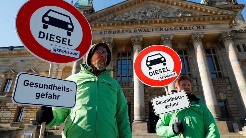 Men in green jackets hold signs in protest of diesel cars.