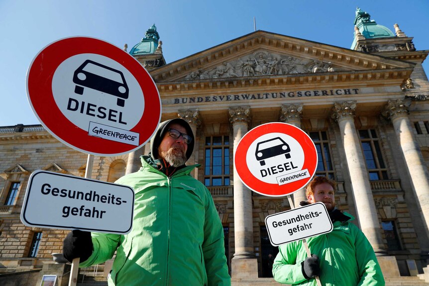 Men in green jackets hold signs in protest of diesel cars.