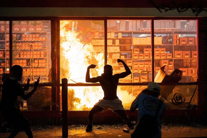 A man poses for photos in front of a fire at a store as it burns