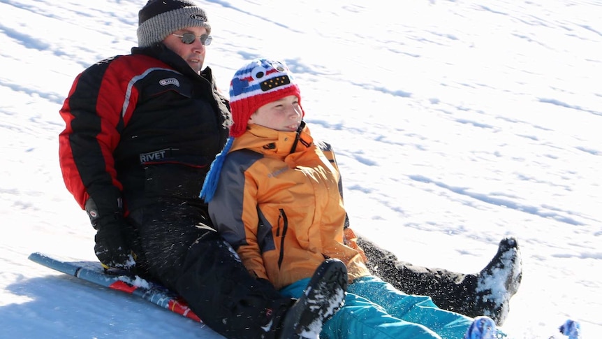 Father and son speed down snow slope on toboggan at Perisher Valley in NSW.