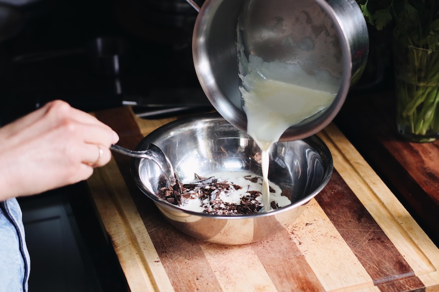 A saucepan of cream is poured into a bowl of grated chocolate.