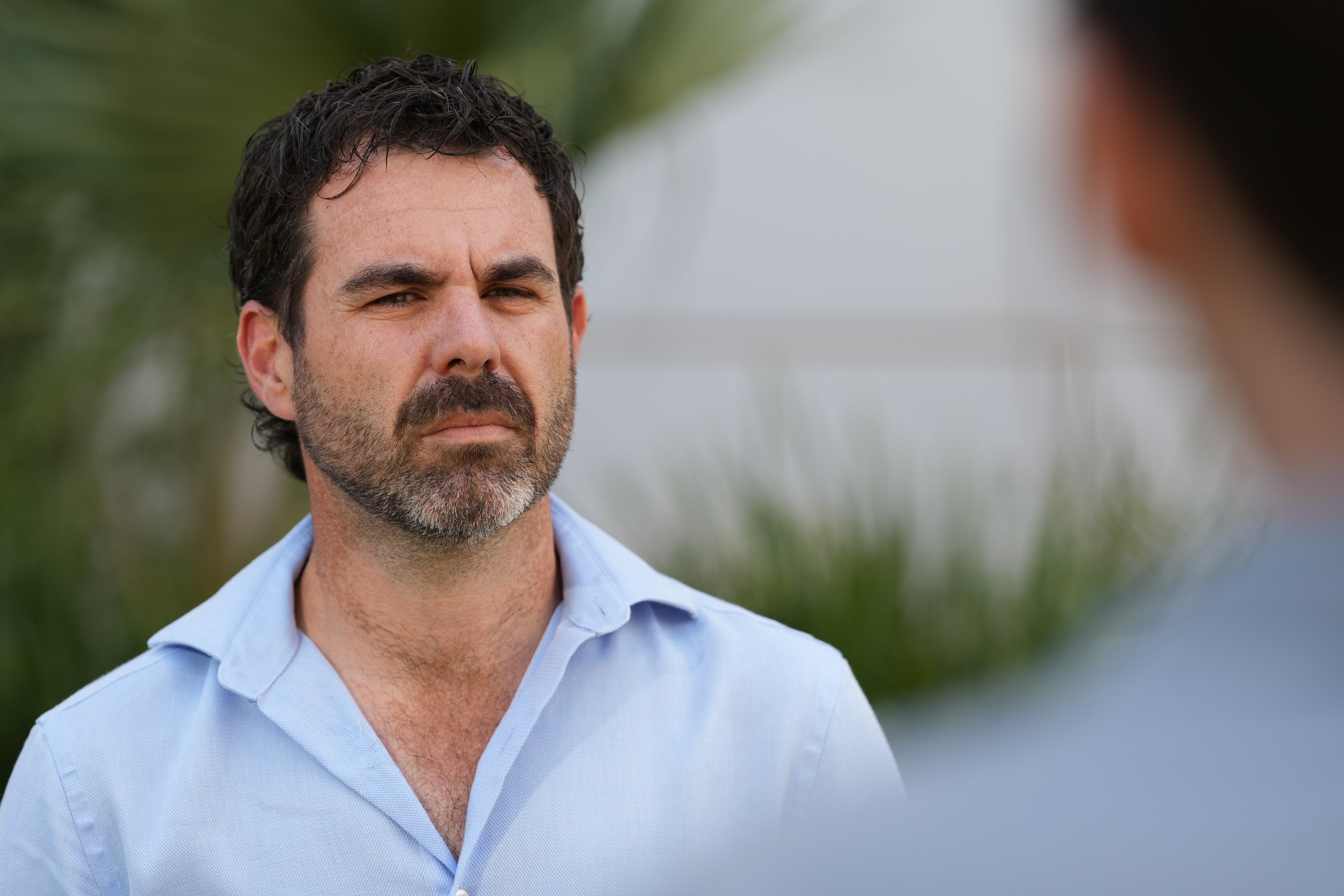 Un hombre con barba y expresión seria se encuentra frente al edificio del Parlamento.