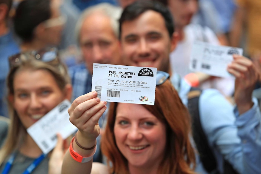 Fans brandish their tickets as they queue outside the Cavern Club in Liverpool