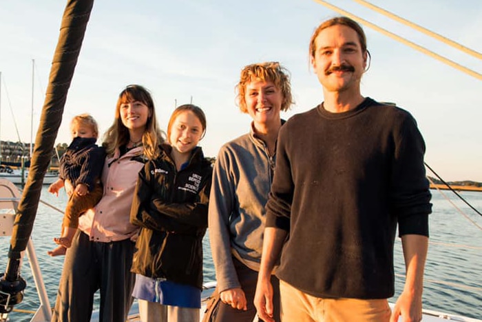 Four people stand on a yacht smiling.