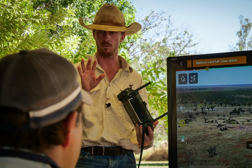 Young cattle grazier holding remote control standing next to screen talking to group of people