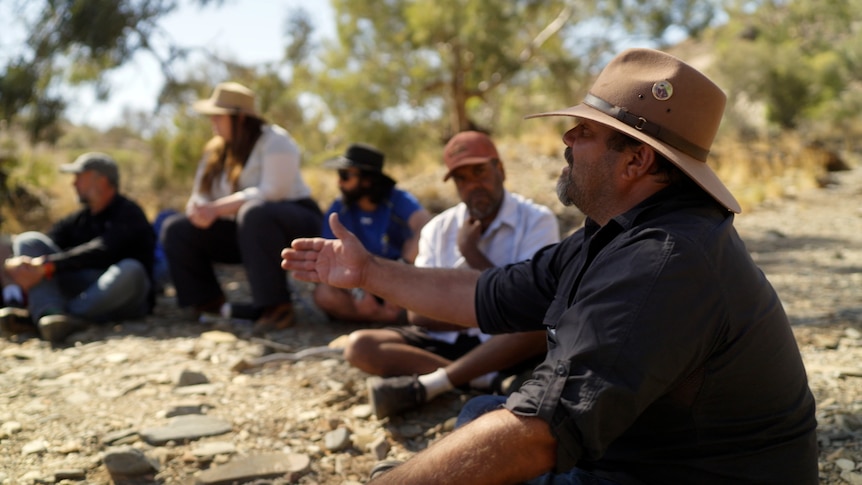 Indigenous man sits with others in outdoor location