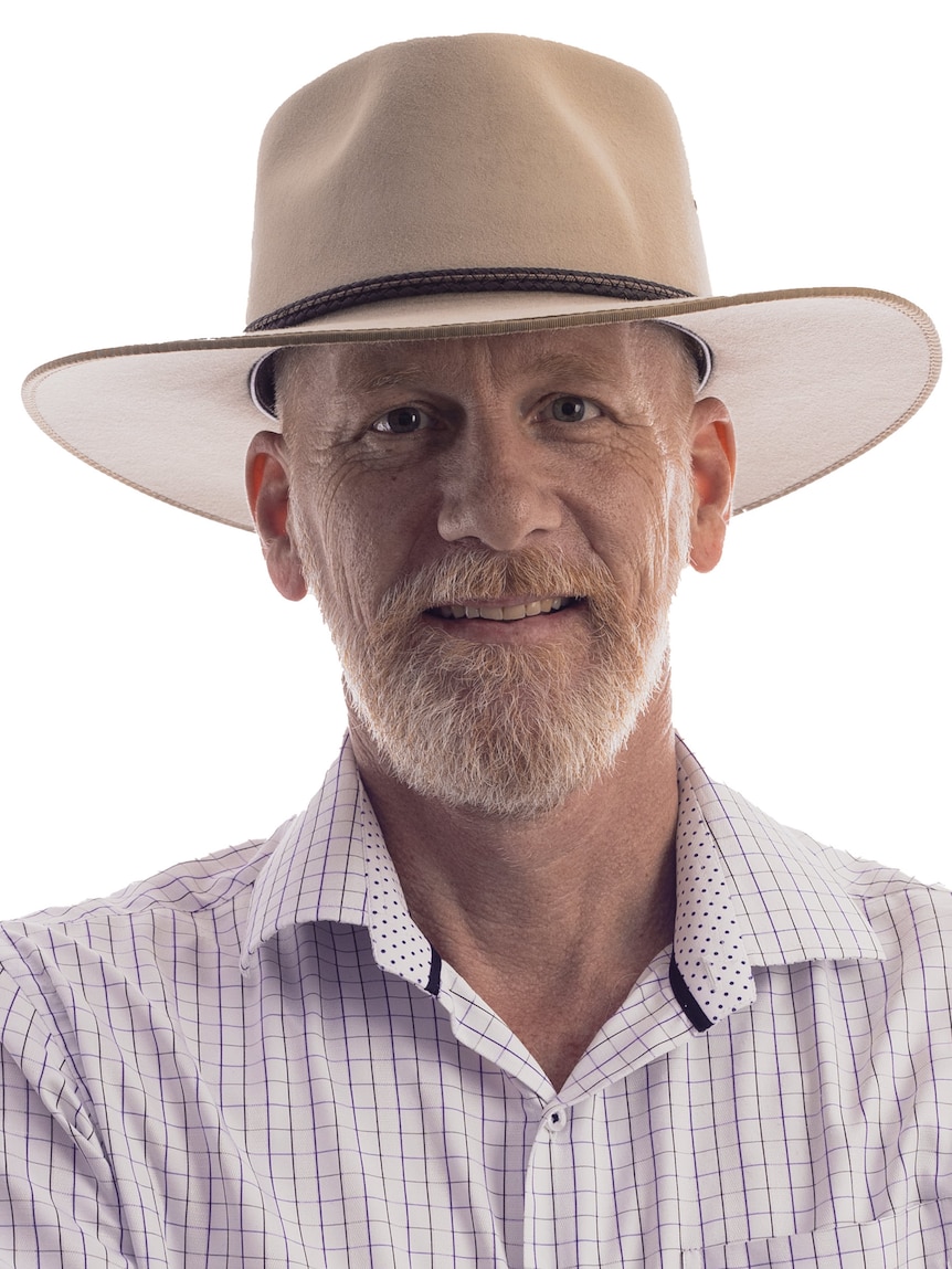 A man in a white akubra smiles at the camera in front of a white background.