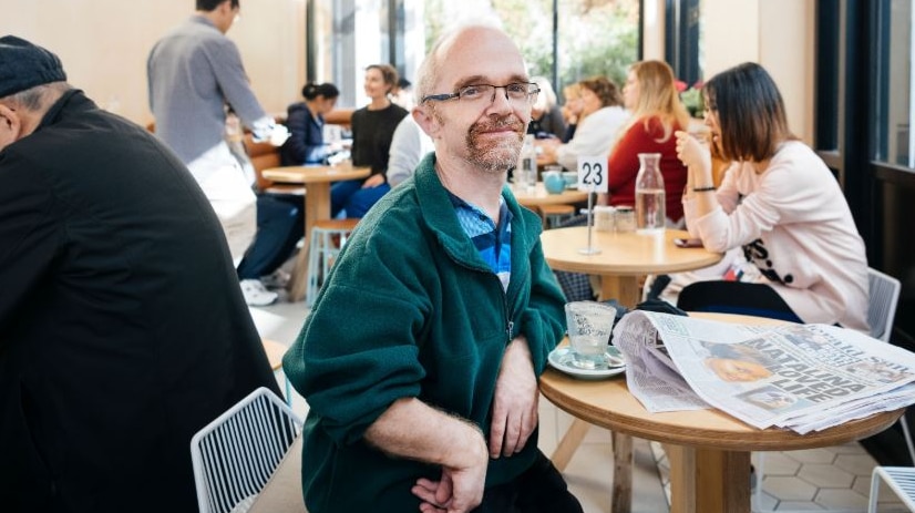 Short statured man Rob Paton sits in a busy cafe