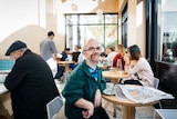 Short statured man Rob Paton sits in a busy cafe