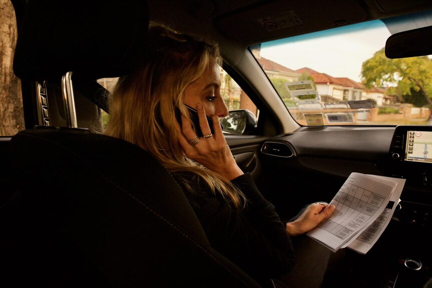 A woman with long blonde hair talks on a mobile phone while sitting in the passenger seat of a car.
