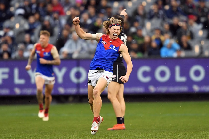 A male AFL player raises his right arm and smiles as he celebrates kicking a goal.