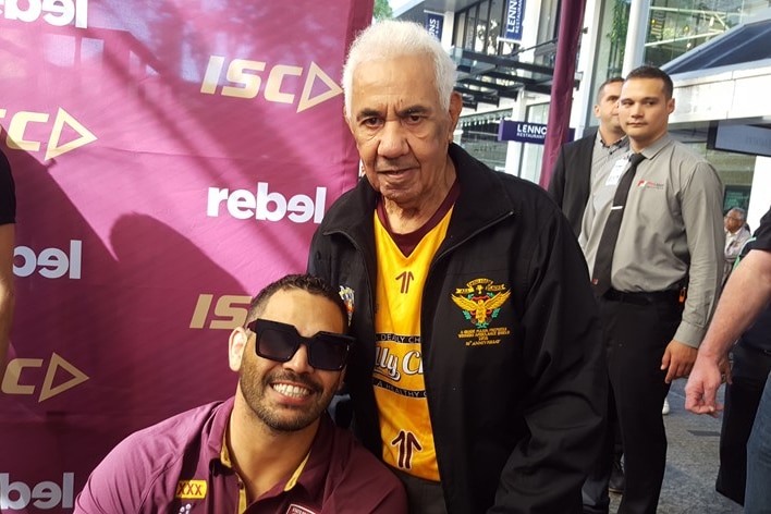 Greg Inglis with sunglasses on sits beside a standing Lionel Morgan 