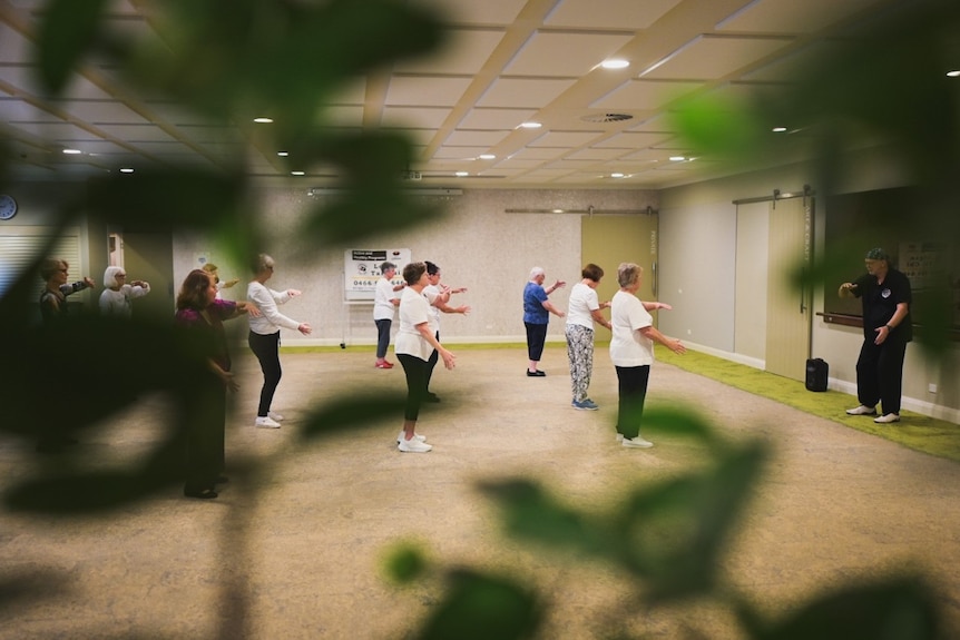 A group of senior do tai chi in a room.
