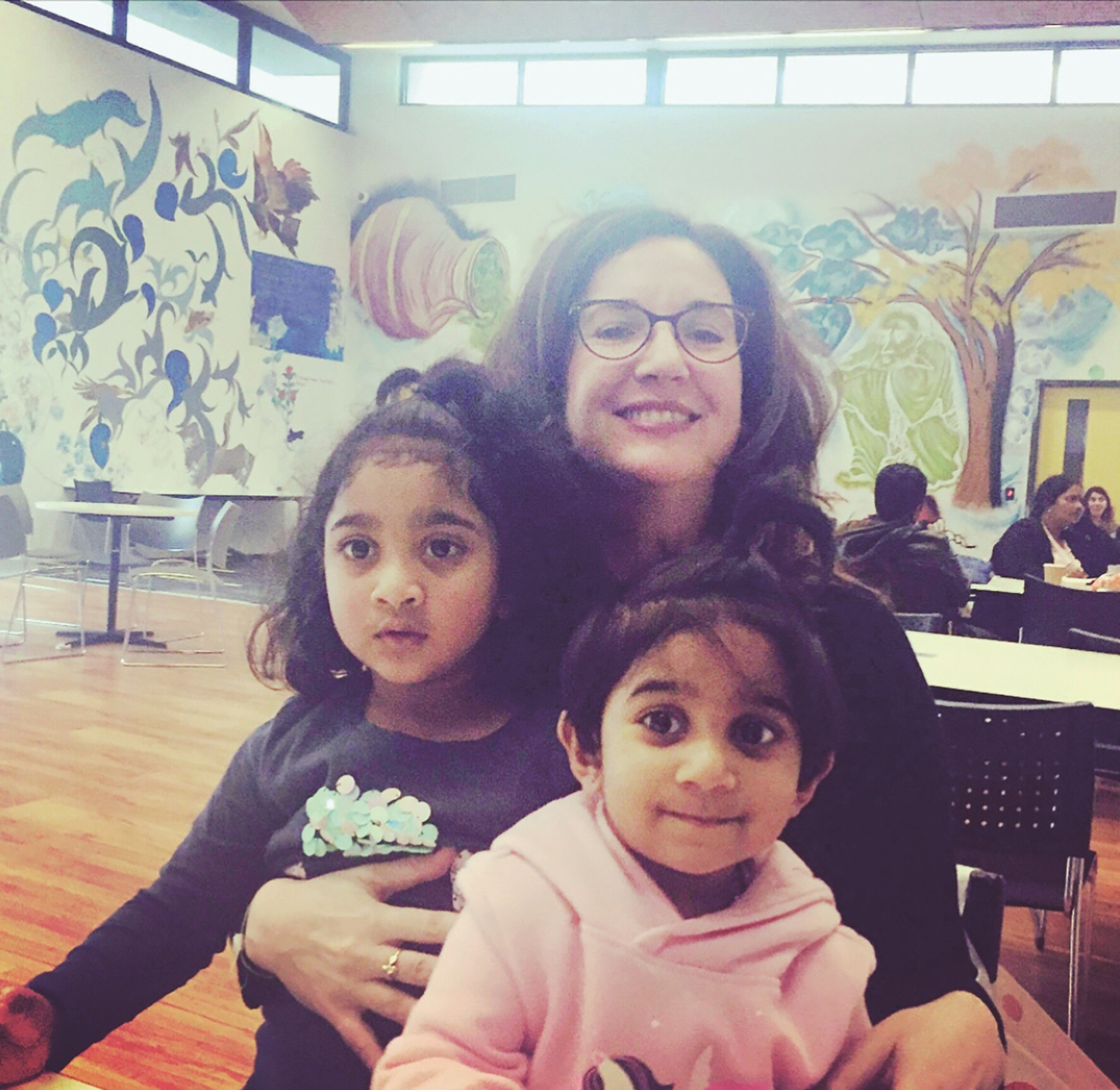 A photo of two small dark-haired girls sitting with a middle-aged white woman