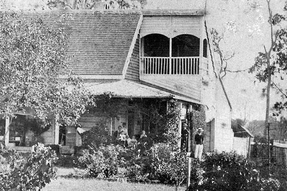 A old photo of a house with people standing on the verandah.