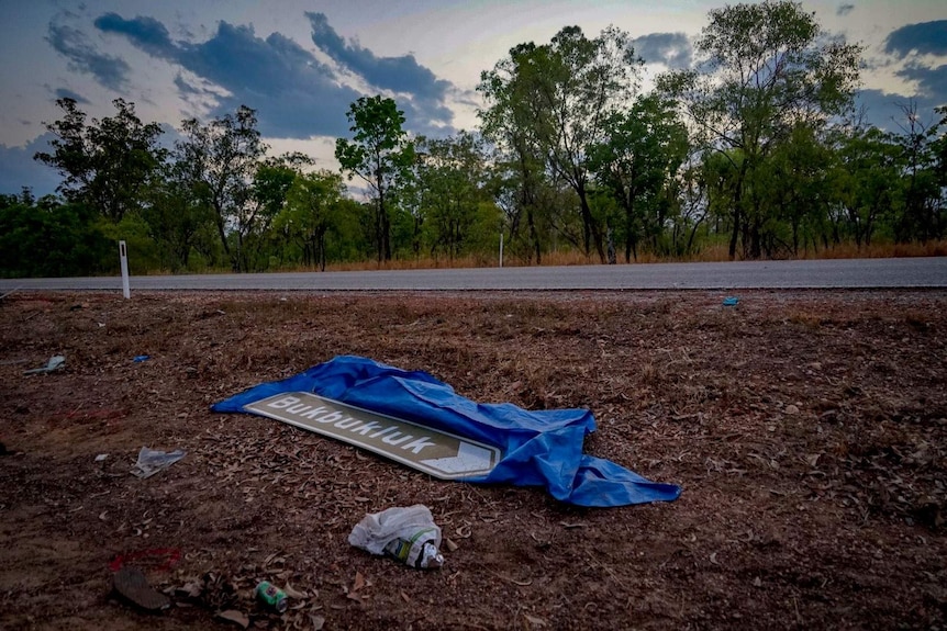 A sign reading "Bukbukluk" lies on the ground by the road