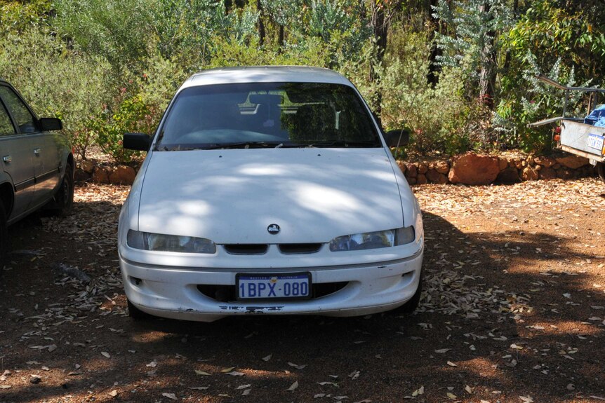 A white Holden Commodore pictured front on with bushland behind it.